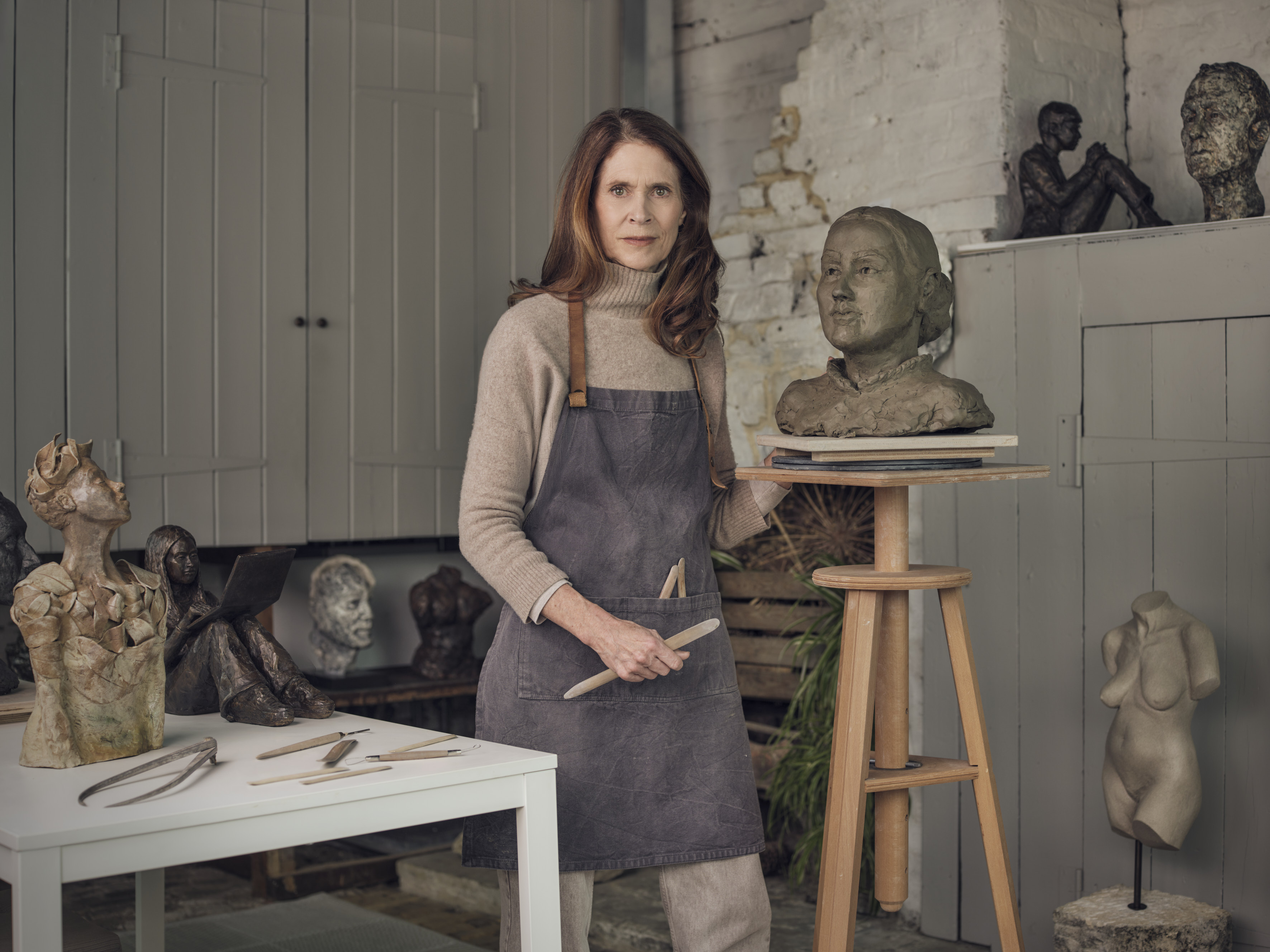 Woman artist standing next to a clay bust on a sculptor's pedestal. ©Gillian Brett